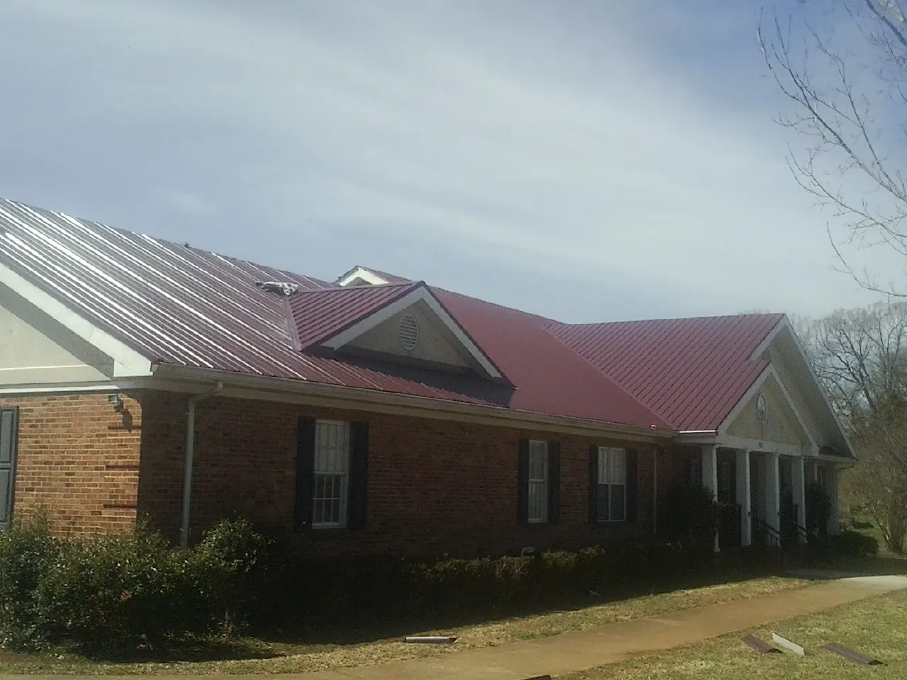 Red metal roof with gabled entries on a long brick building, from a Hail Damage Roof Repair job in Hallam